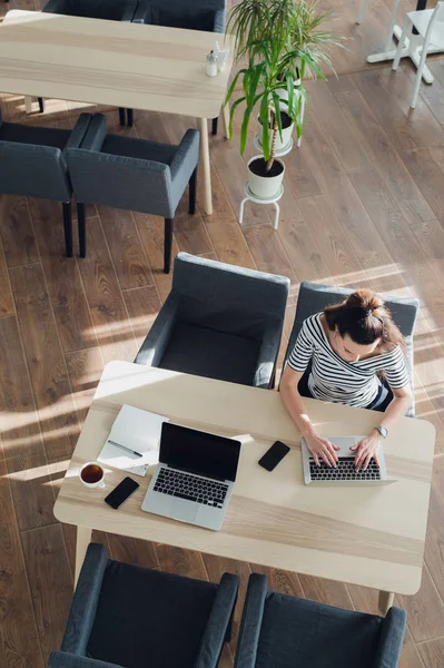 Draufsicht oder Draufsicht einer schönen Frau, die an einem Tisch sitzt und an ihrem Laptop arbeitet. die Sonne wirft Schatten auf den Holzboden. — Stockfoto