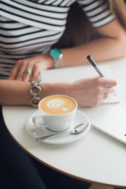 Kağıt, cappucciono fincan üzerine notlar ve laptop ayakta bir tabloda bir kafede yapma el yakın çekim resim.