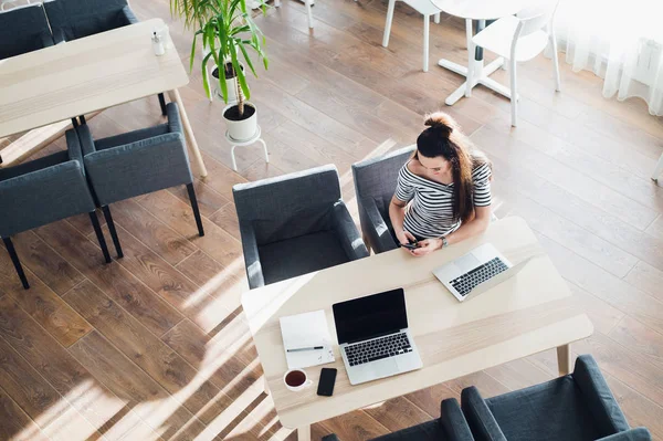 Bovenaanzicht van het vrouwtje haar laptop gebruikt in een café. Overhead schot van jonge vrouw zitten aan een tafel met een kopje koffie en mobiele telefoon surfen op het net op haar laptopcomputer. — Stockfoto