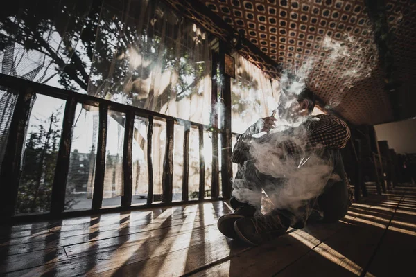 Vaping joven hombre produce vapor en la silueta de la puesta del sol — Foto de Stock