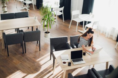 Yan görünümü. Tablo ve not defterindeki not almak oturan genç iş kadını. Masada dizüstü bilgisayar, akıllı telefon ve kahve var. Öğrenci öğrenme Online. Blogger.