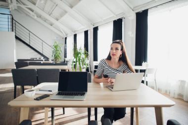 Modern Ofis Masası, dizüstü bilgisayar ve telefon üzerinde çalışıyor, uzağa bakarak, hakkında bir yazı, tam zamanlı blogcu için ilham arayan düşünme yetişkin kadın.