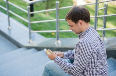 Bir merdiven üzerinde oturan yakın çekim mobil akıllı telefonunu açık adam kullanır