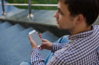 Bir merdiven üzerinde oturan yakın çekim mobil akıllı telefonunu açık adam kullanır