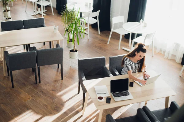 Yan görünümü. Tablo ve not defterindeki not almak oturan genç iş kadını. Masada dizüstü bilgisayar, akıllı telefon ve kahve var. Öğrenci öğrenme Online. Blogger.