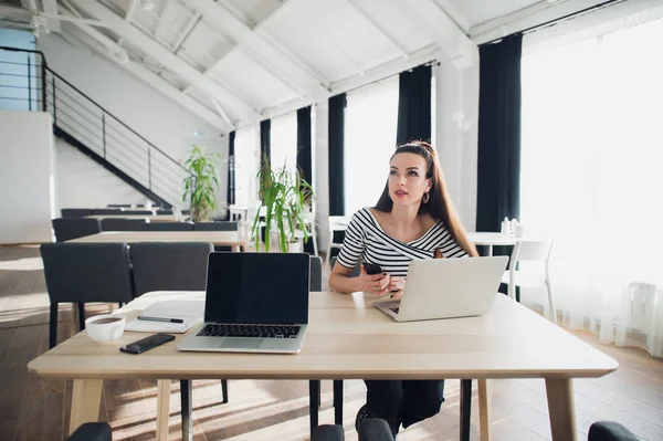 Volwassen vrouw op een moderne kantoor bureau, bezig met laptop en telefoon, op zoek weg, nadenken over een post, full-time blogger, op zoek naar inspiratie. — Stockfoto