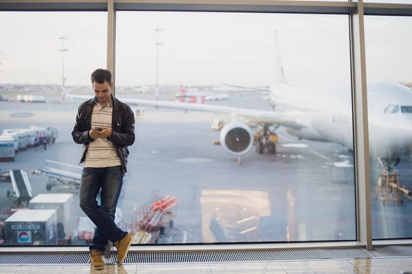 Reisende im Flughafenterminal. Junger Mann benutzt Handy und wartet auf seinen Flug. — Stockfoto