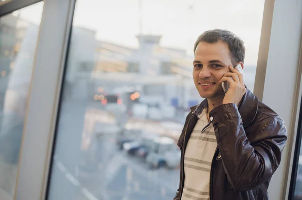 Jeune voyageur à l'aéroport, veste en cuir sur son smartphone — Photo