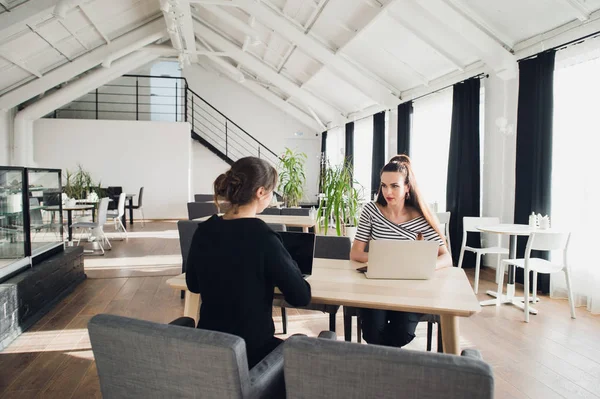 Equipe de negócios do sexo feminino tendo uma reunião em conjunto para discutir papelada sentado em uma mesa tendo uma discussão. Duas mulheres de negócios sentadas em uma mesa com laptops e uma perguntando a outra . — Fotografia de Stock