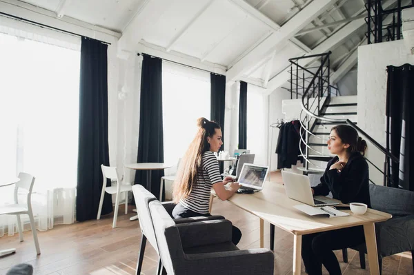 As mulheres de negócios discutem na reunião no escritório moderno. Duas colegas de trabalho sentadas à mesma mesa com laptops . — Fotografia de Stock