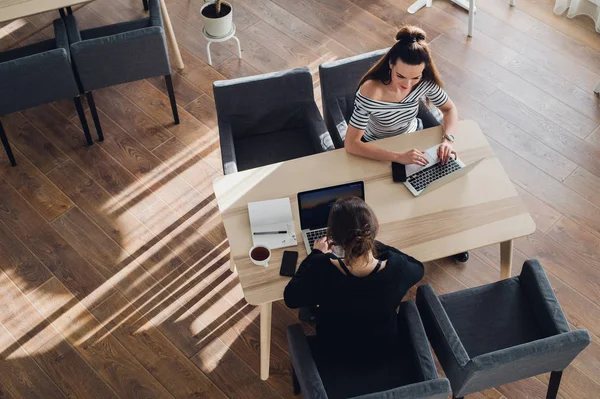 Visão geral da jovem mulher usando um smartwatch trabalhando em seu laptop em um café. Top vista tiro de fêmea sentado em uma mesa com um telefone nas proximidades e navegar na internet . — Fotografia de Stock