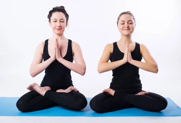 Two women doing yoga and meditating in lotus position isolated on white background. — Stock Photo, Image