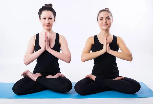 Two women doing yoga and meditating in lotus position isolated on white background. — Stock Photo, Image