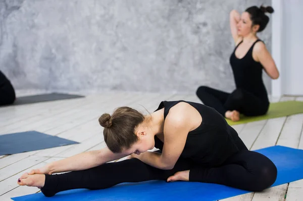Shot of young women warming up before yoga session. Young people sitting on exercise mat in yoga class. — Stock Photo, Image