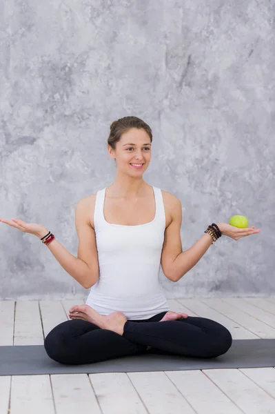 Happy sport kvinna som håller apple sitter på en yogamatta över grå bakgrund — Stockfoto