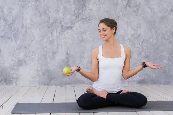 Caucasian beautiful healthy athletic sportive girl eat green apple after the training and looking at camera