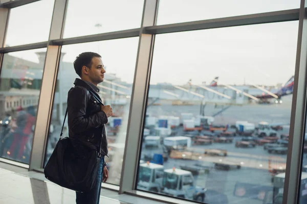 Conceito de viagem com jovem no interior do aeroporto com vista para a cidade e um avião voando por . — Fotografia de Stock