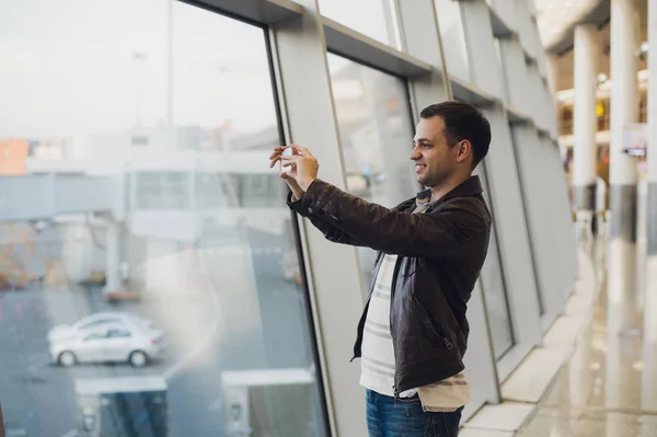 Traveler with mobile phone at the airport taking picture of his aircraft. Air Traffic Control facilities at the background — Stock Photo, Image