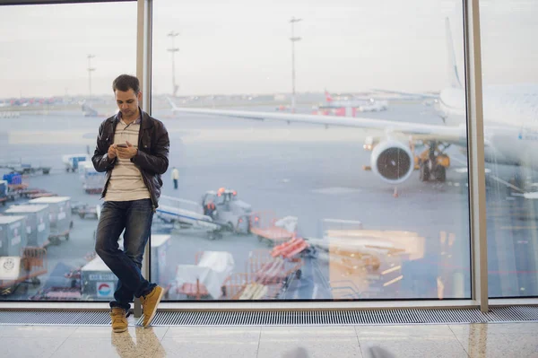 Reisende im Flughafenterminal. Junger Mann benutzt Handy und wartet auf seinen Flug. — Stockfoto
