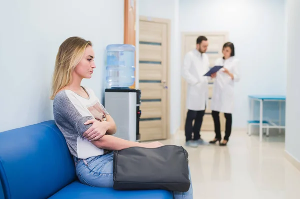 Genç kadın iki doktor bir kağıt üzerinde konuşma sırasında bekleyen hastane koridor az gergin oturma doldurma — Stok fotoğraf