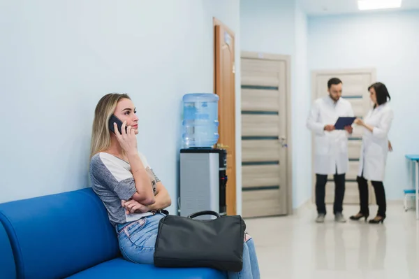 Woman patient in speaking at the mobile phone in hospital waiting room. — Stock Photo, Image