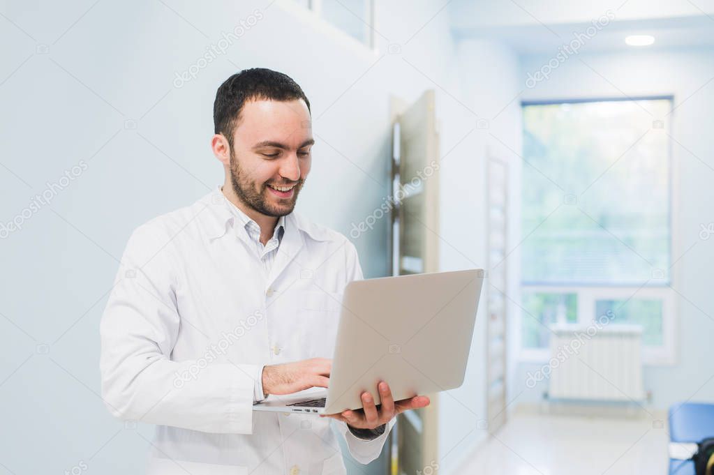 Portrait of cheerful doctor sitting at the desk working on laptop