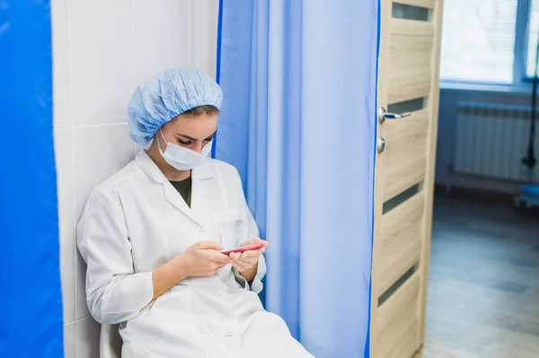 Mujer joven médico sentado con su teléfono móvil durante el descanso — Foto de Stock