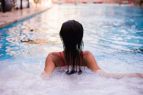 Mujer de pelo negro acostada en el borde del bassin de una piscina con agua azul profunda y fresca ondulada — Foto de Stock