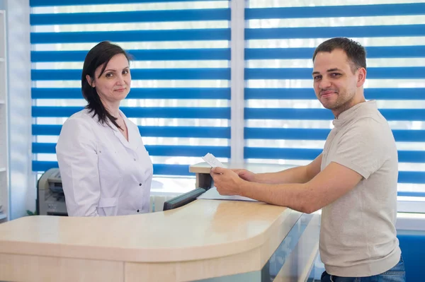 Recepcionista feminina adulta média recebendo cartão do paciente na clínica odontológica — Fotografia de Stock