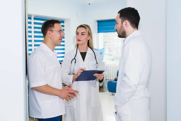 Vista de ángulo alto de tres médicos con batas blancas conversando en la sala del hospital —  Fotos de Stock