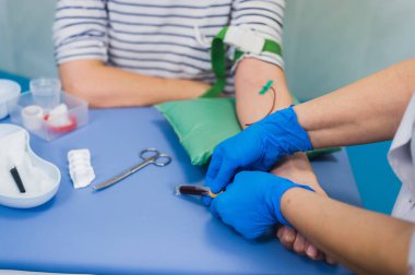 Beyaz parlak oda tablo Beyaz önlük tıbbi üniformalı kadın doktor tarafından oldukça genç sarışın kadınla hazırlık kan testi için. Hemşire hasta kol damarı iğne boş tüp ile delip geçiyor..