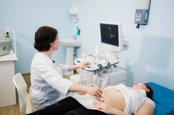 Doctor using ultrasound and screening stomach of pregnant woman.