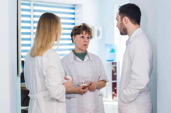 Médico maduro discutiendo con enfermeras en un hospital de pasillo. Doctor discutiendo el estado del caso del paciente con su personal médico después de la operación . — Foto de Stock