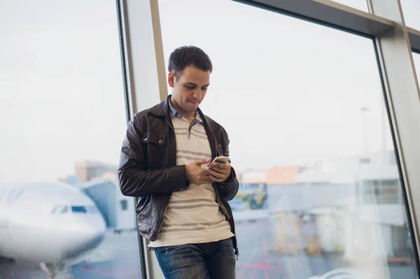 Traveler inuti flygplatsterminalen. Ung man med hjälp av mobiltelefon och väntar på sin flight. — Stockfoto