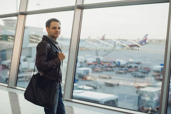 Reizen concept met jonge man in luchthaven interieur met uitzicht op de stad en een vliegtuig vliegt door. — Stockfoto