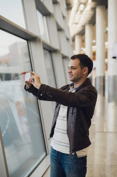 Viajero con teléfono móvil en el aeropuerto tomando fotos de su avión. Instalaciones de control del tráfico aéreo en segundo plano —  Fotos de Stock