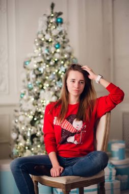 Mutlu genç kadın Noel ağacının yanında oturuyor..
