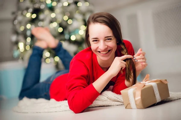 Красива щаслива молода жінка лежить на підлозі, тримаючи різдвяний подарунок — стокове фото