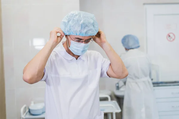 Giovane medico durante la preparazione per l'operazione. Assistente del chirurgo con maschera chirurgica in sala operatoria dell'ospedale . — Foto Stock