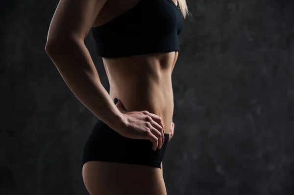 Widok z boku z mięśni fitness kobiece kobieta model stojący na czarnym tle. Młoda kobieta na sobie biustonosz sportowy, patrząc w dół w myśl. — Zdjęcie stockowe