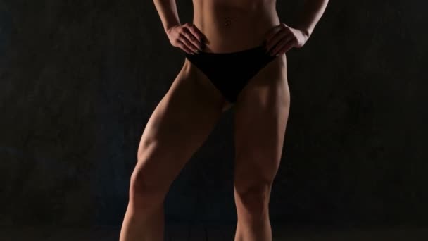 Dziewczyna Brunetka fitness sexy sport zużycie z doskonałego ciała w siłowni pozowanie przed treningiem zestaw. Kobieta pokazując mięśnie nóg na ciemnym tle. — Wideo stockowe