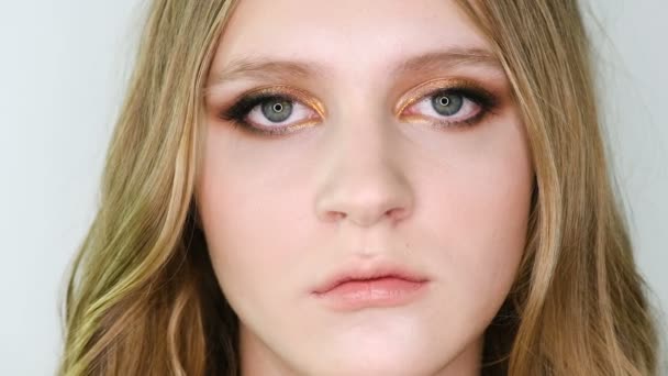 Close-up portret van mooie jonge vrouw gezicht met heldere bronze make-up op zoek op camera, dan aan de voorkant. Meisje weergegeven: oog make-up — Stockvideo