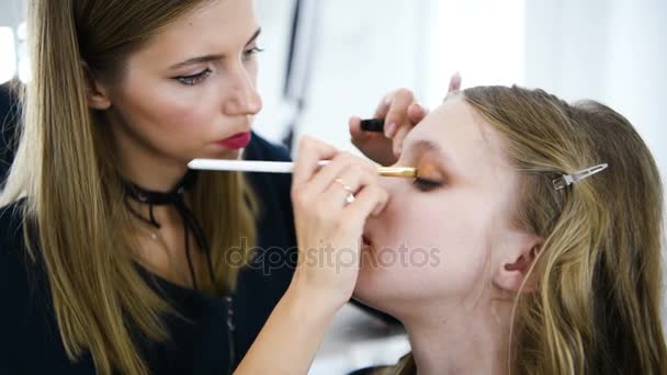 Jovem mulher aplicando maquiagem ao modelo no salão — Vídeo de Stock