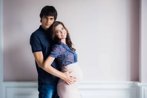 Bella giovane coppia in attesa di bambino stare davanti al muro a casa . — Foto Stock