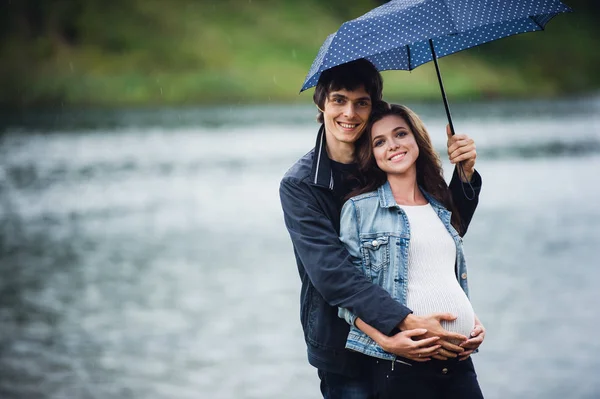 Donna incinta e uomo che tengono un ombrello al parco nella giornata secca all'aperto — Foto Stock