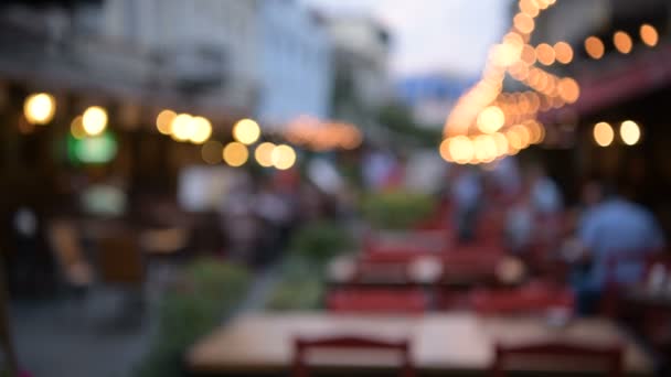 Wazig zicht op straat café gedecoreerd met lampen en mensen lopen door — Stockvideo