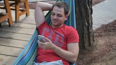 bir hamakta dinlenirken mobil akıllı telefon kullanan adam