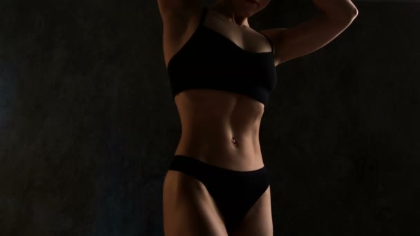 Mujer joven muscular en el estudio sobre fondo oscuro muestra los diferentes movimientos y partes perfectas del cuerpo. Abdominales y glúteos de cerca — Vídeos de Stock
