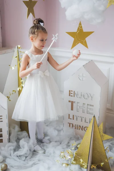 Little happy fairy or angel with magic wand on Holiday theme. Portrait of pretty caucasian little angel wearing white dress and holding magic stick