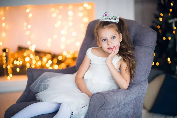 Schattig klein meisje in slimme witte jurk Kerstmis rond de open haard die versierd met vakantie slinger — Stockfoto